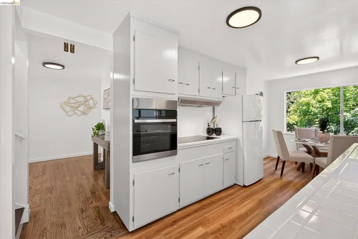 Kitchen featuring white cabinetry, stainless steel built-in oven, wood-finish flooring, and ample natural light from a large window
