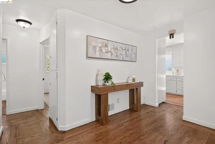 Entryway featuring wood-finish flooring, white walls, and a view into a kitchen space with white cabinetry