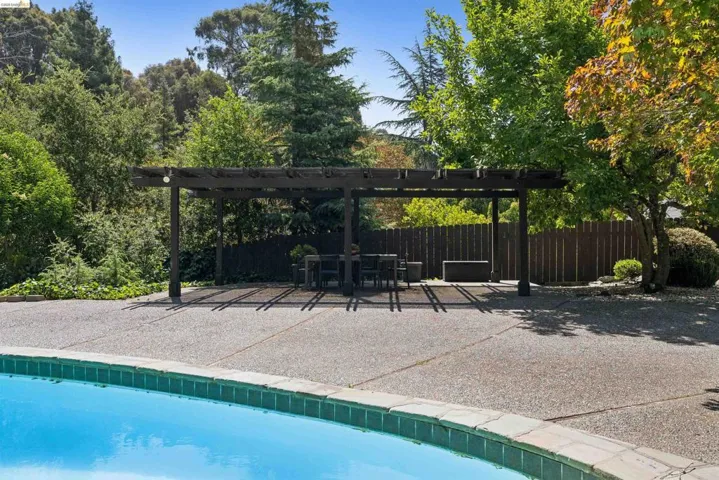 Expansive backyard featuring a large swimming pool with tile coping, an exposed aggregate concrete patio, and a substantial wooden pergola