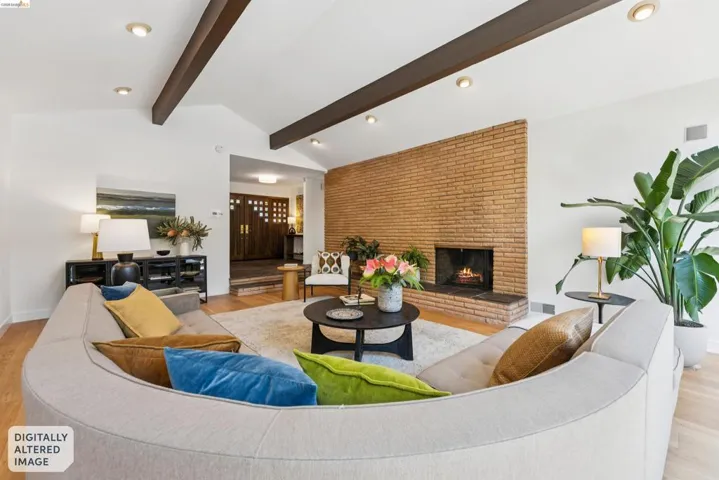 Vaulted ceilings with exposed wood beams define this living area, featuring a brick-clad fireplace with a raised hearth