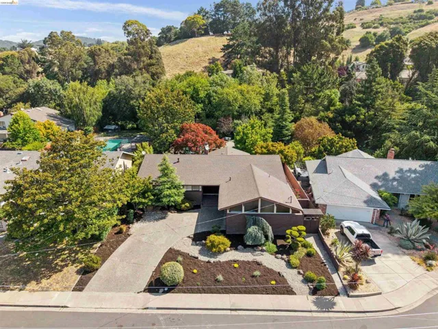 Mid-century modern home with a prominent gabled roofline, a concrete driveway, and established front yard landscaping