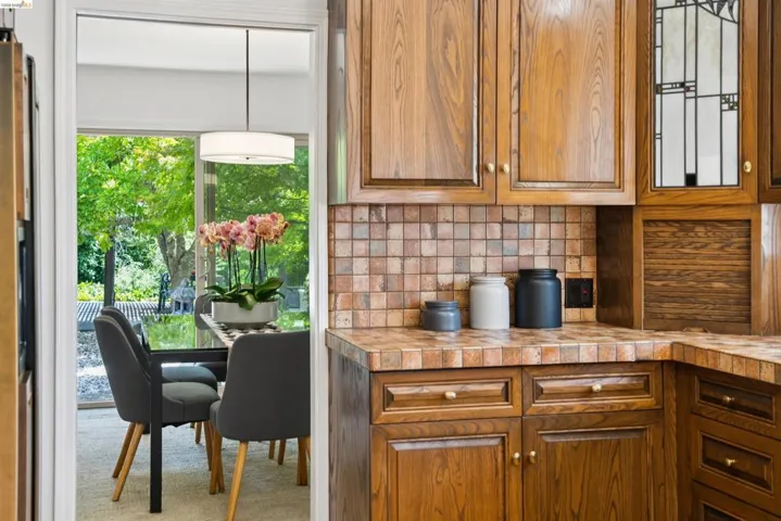 Wood cabinetry with decorative hardware, a tiled countertop, and a square mosaic tile backsplash