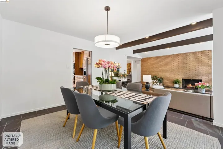 Open concept living area with exposed ceiling beams and a brick accent wall featuring a fireplace