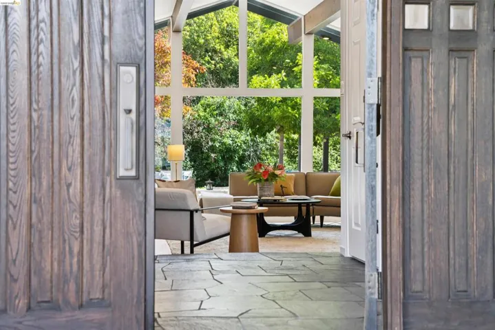 Spacious interior featuring a wall of full-height windows, vaulted ceilings with exposed beams, and stone-finish flooring