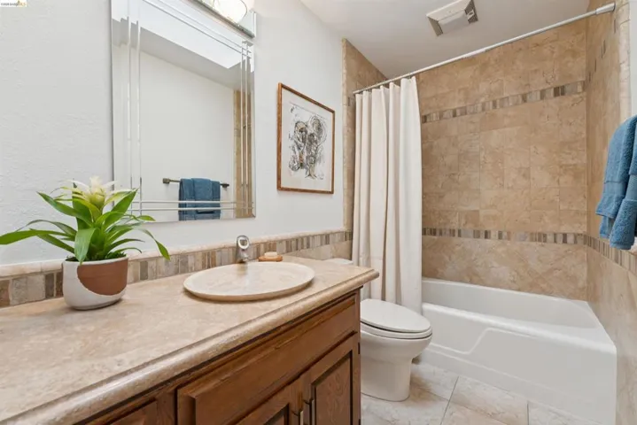Bathroom featuring a built-in bathtub with tiled surround, wood-finish vanity with an oval vessel sink, and a framed mirror