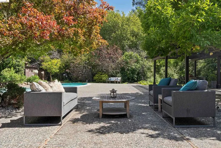 Expansive stone patio featuring a perimeter swimming pool and diverse mature landscaping