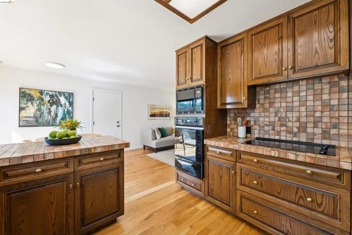 Kitchen featuring wood cabinetry, integrated appliances, a tiled backsplash, a built-in cooktop, and wood-finish flooring