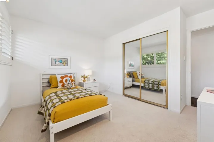 Light-filled bedroom featuring an expansive mirrored closet, neutral carpeting, and white plantation shutters
