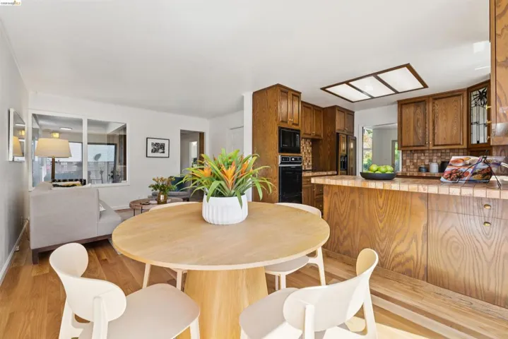 Open-concept living space featuring wood-finish flooring, a kitchen with rich wood cabinetry, a tiled backsplash, and an integrated kitchen island with tiled countertop