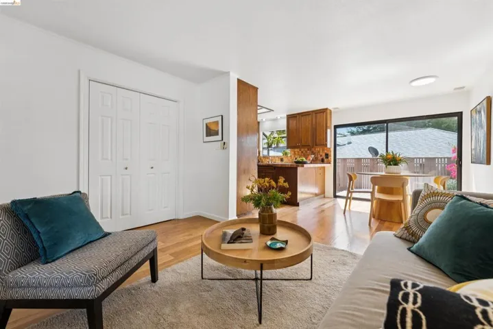 Open-concept living space featuring wood-finish flooring, white walls, built-in bi-fold closet doors, a kitchen bar, and sliding glass patio doors