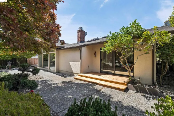 Exterior stucco finish with a prominent brick chimney, multiple sliding glass doors, a wooden deck, and a gravel patio area