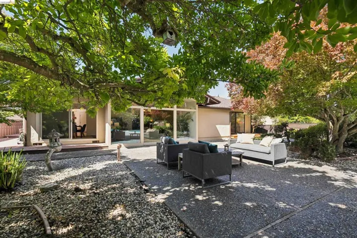 Expansive backyard with a large stone patio, mature trees, and gravel landscaping