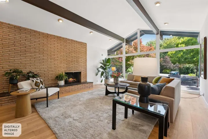 Vaulted ceiling living area featuring an exposed brick fireplace, light wood-finish flooring, and expansive windows
