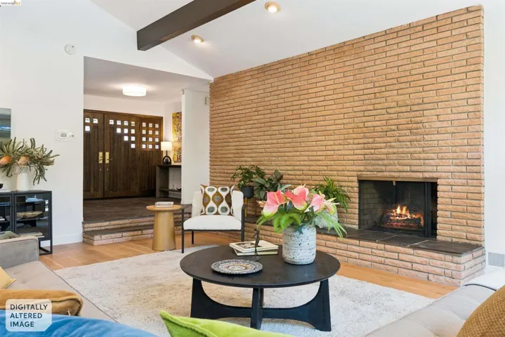 Living area featuring a floor-to-ceiling brick fireplace with hearth, vaulted ceilings with exposed beams, wood-finish flooring, and a recessed entry with double doors