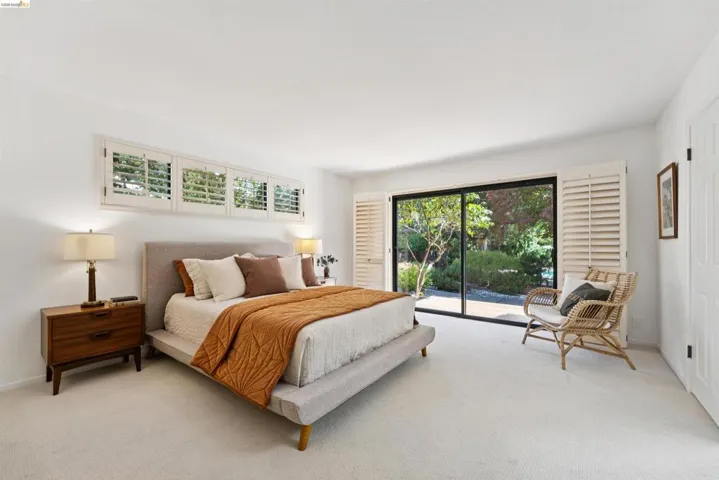 Bright bedroom featuring a large sliding glass door, white plantation shutters, and a wall of transom windows