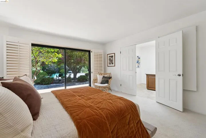 Bedroom featuring expansive glass sliding doors, white plantation shutters, neutral carpeting, and a pair of six-panel interior doors