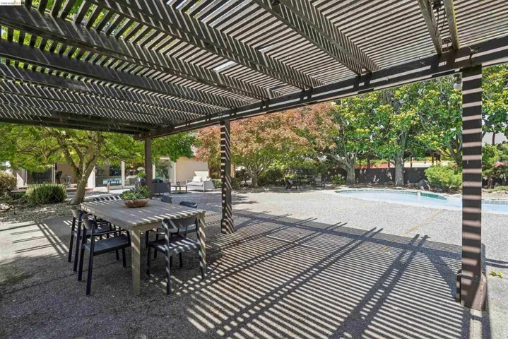 Expansive outdoor living area featuring a large pergola, extensive paved patio, mature trees, and a swimming pool
