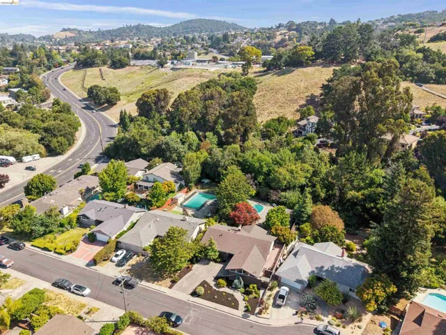 Residential neighborhood featuring a curvilinear road, mature trees, and a distant hillside backdrop