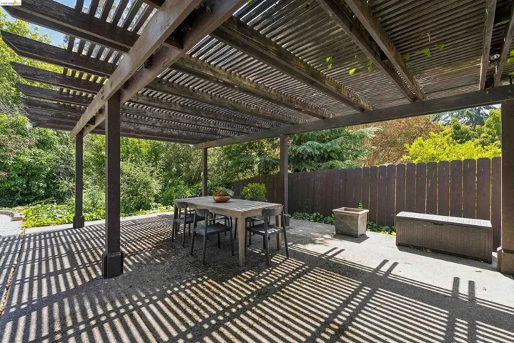 Spacious outdoor patio featuring a slatted wood pergola, concrete flooring, and a privacy fence