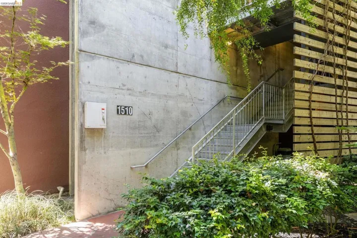 Exterior featuring concrete facade, metal staircase with handrails, wood slat detailing, and mature landscaping