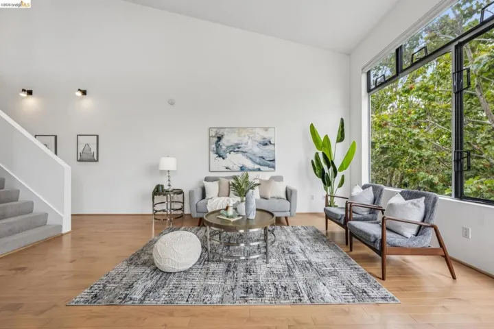 Spacious living area featuring high ceilings, wood-finish flooring, a wall of large windows, and a carpeted staircase