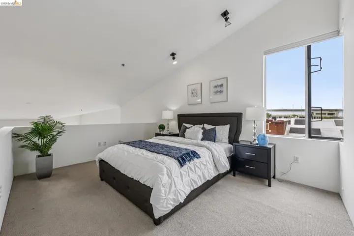 Carpeted loft space featuring an angled ceiling, track lighting, and a large window