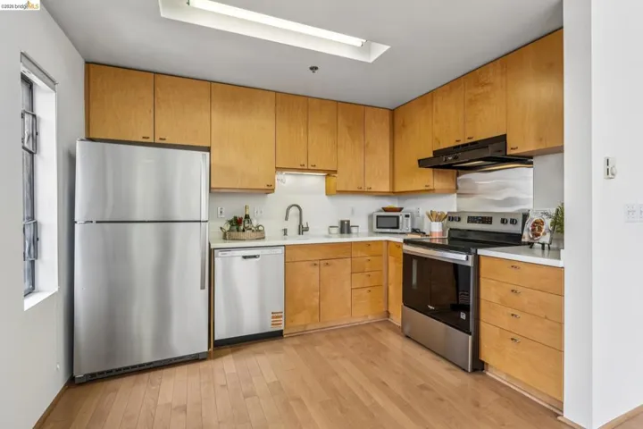 Kitchen featuring natural wood cabinetry, stainless steel appliances, light-toned countertops, and wood-finish flooring