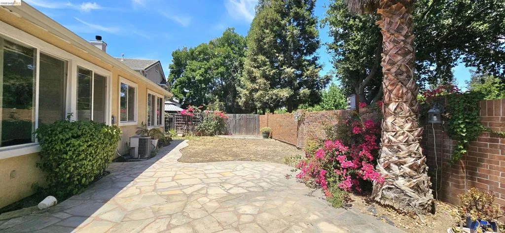 Expansive flagstone patio with a large palm tree, surrounding flowering shrubs, and a brick privacy wall