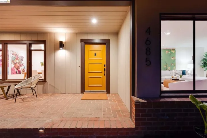 Brick paver porch with integrated lighting, a vibrant yellow entry door, and a modern wall sconce