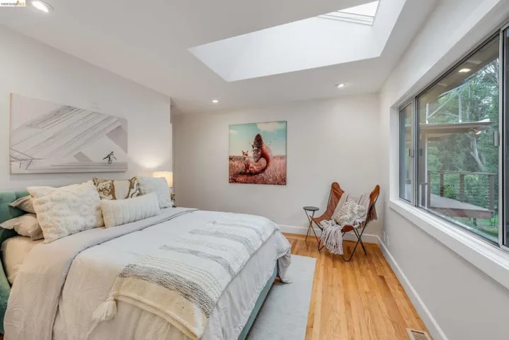 Bright room featuring light wood-finish flooring, a large window, a skylight, recessed lighting, and white baseboards