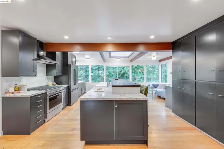 Modern kitchen featuring dark cabinetry, stainless steel appliances, a center island with a stone countertop, light wood-finish flooring, and recessed lighting