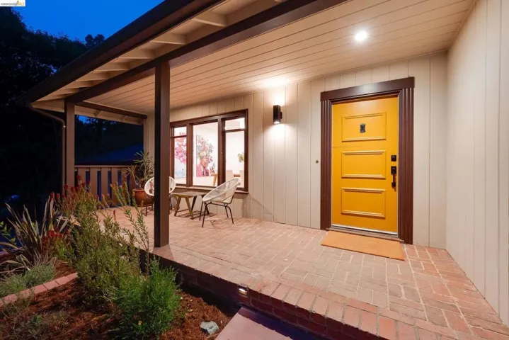 Inviting covered porch with brick flooring, a vibrant yellow entry door, and dark wood trim