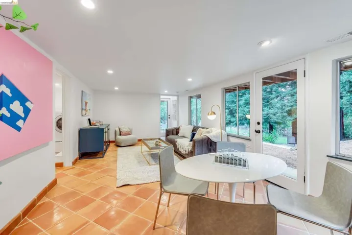 Spacious room featuring terra cotta tile flooring, multiple windows, a glass-paned door, recessed lighting, and a dedicated laundry area with stacked appliances