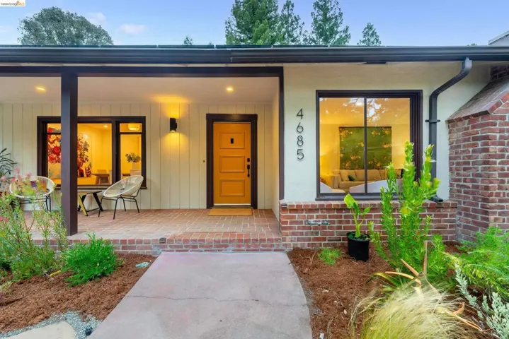 Front facade featuring a prominent yellow entry door, brick base, and a covered porch with a brick-finish floor