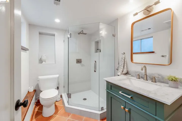 Contemporary bathroom featuring a frameless glass shower enclosure with a rain shower head, a floating vanity with a marble-finish countertop, and gold-toned hardware