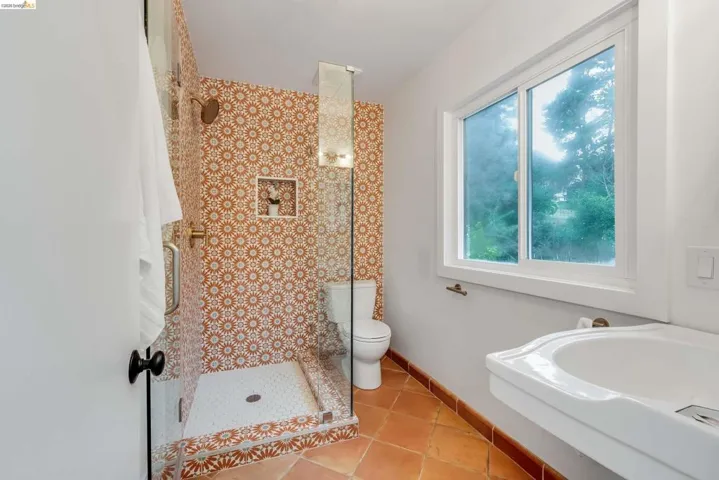 Walk-in shower with patterned tile surround and integrated niche, glass enclosure, and brass fixtures