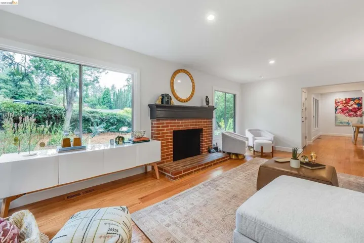 Bright living area featuring a brick fireplace with a dark mantel, large picture windows, recessed lighting, and hardwood flooring