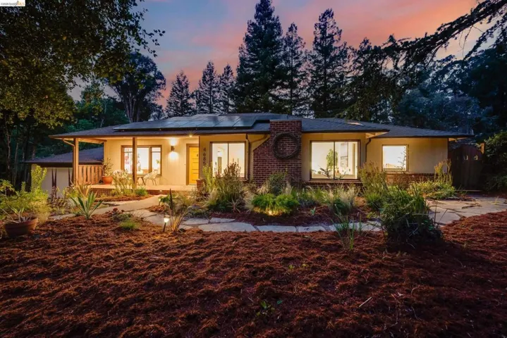 Single-story residence featuring a covered front porch, solar panels, and a brick-clad chimney with an integrated circular detail