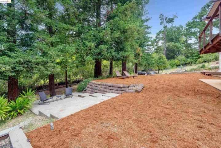 Expansive outdoor area featuring a wood chip ground cover, concrete patio, and a tiered retaining wall