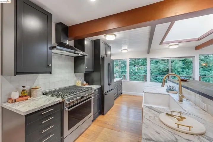 Gourmet kitchen featuring dark shaker-style cabinetry, stainless steel range with hood, white subway tile backsplash, and light-toned stone countertops