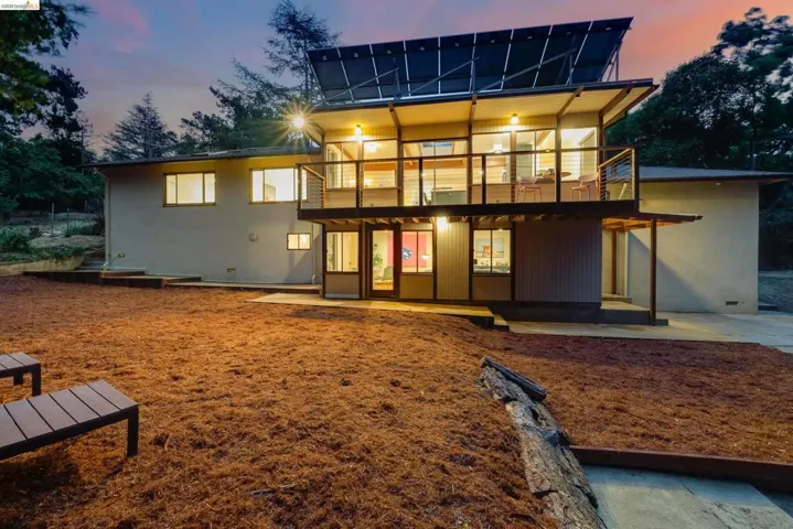 Multi-level contemporary exterior featuring a second-story balcony with cable railing, expansive windows, and upper-level solar panels