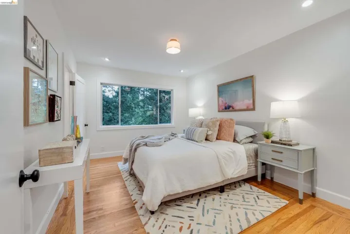 Bright bedroom featuring hardwood flooring and a large window overlooking lush greenery