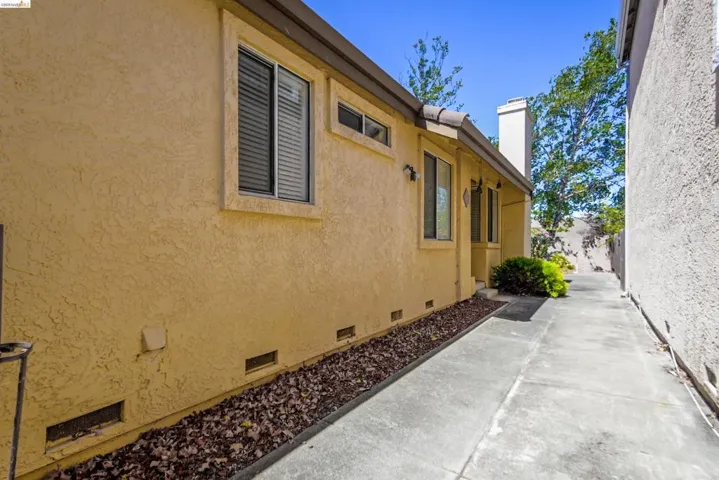 Stucco exterior with multiple windows, concrete walkway, and a chimney feature