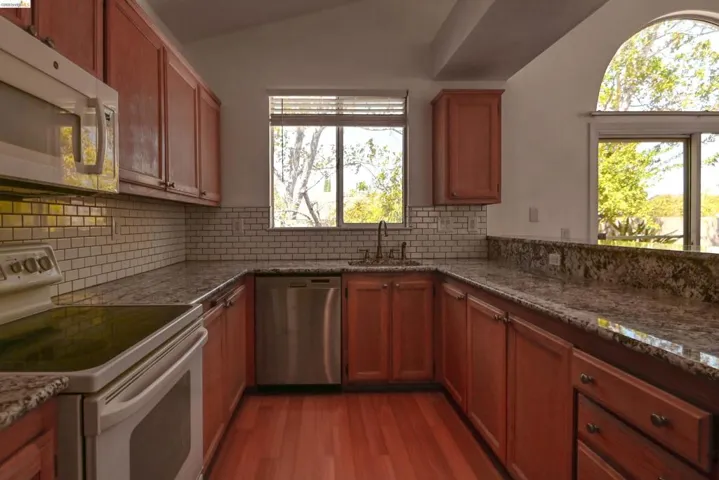 Kitchen featuring warm wood cabinetry, granite countertops, subway tile backsplash, and wood-finish flooring