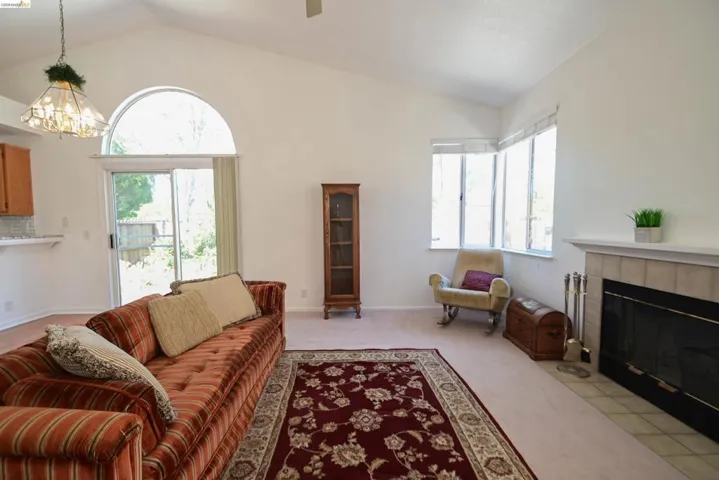 Vaulted ceiling living space featuring a fireplace with a tile surround and mantel, a sliding glass door with an arched transom window, and bay windows