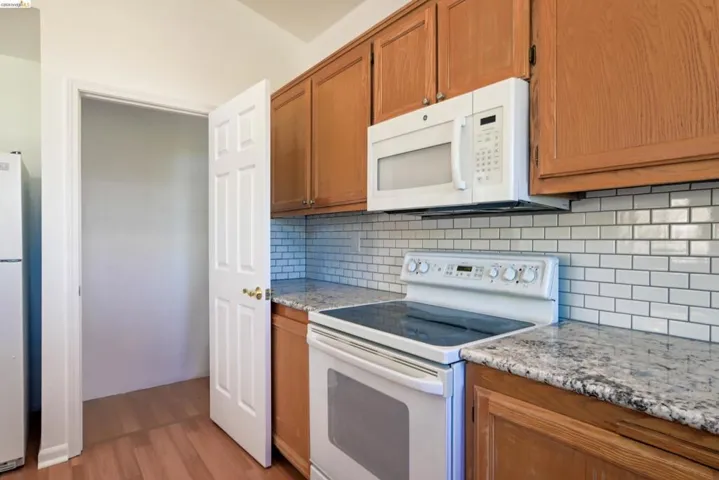 Kitchen featuring wood-finish cabinetry, granite-style countertops, a subway tile backsplash, and a built-in microwave