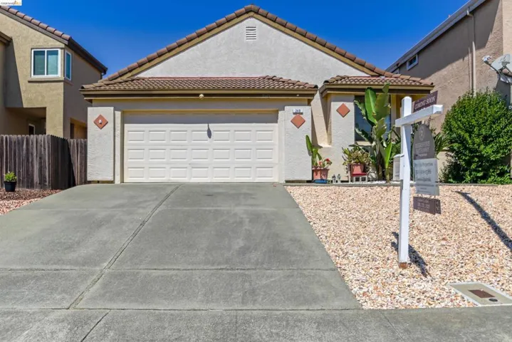 Stucco exterior featuring a two-car garage, tile roof, concrete driveway, and low-maintenance gravel landscaping