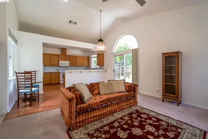 Vaulted ceiling living area with a kitchen passthrough bar, wood-finish flooring in the kitchen, and sliding glass door access to the exterior
