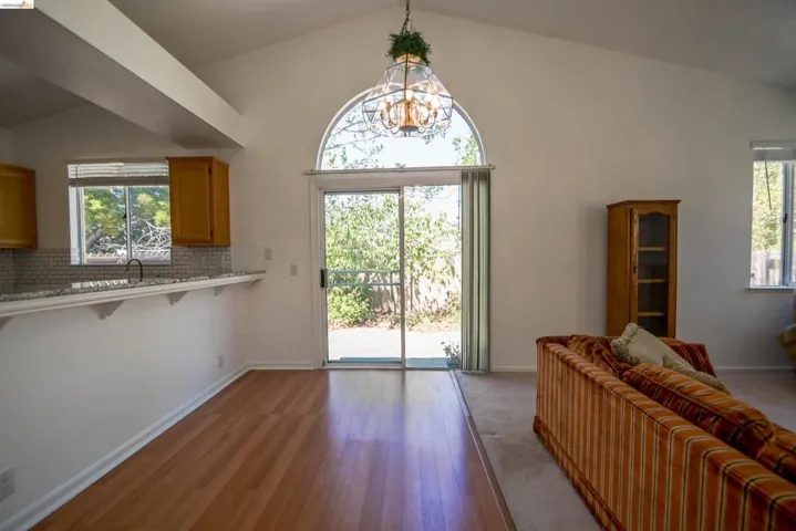 Vaulted ceilings with a decorative chandelier, wood-finish flooring, and a kitchen pass-through featuring a granite-style countertop and tile backsplash