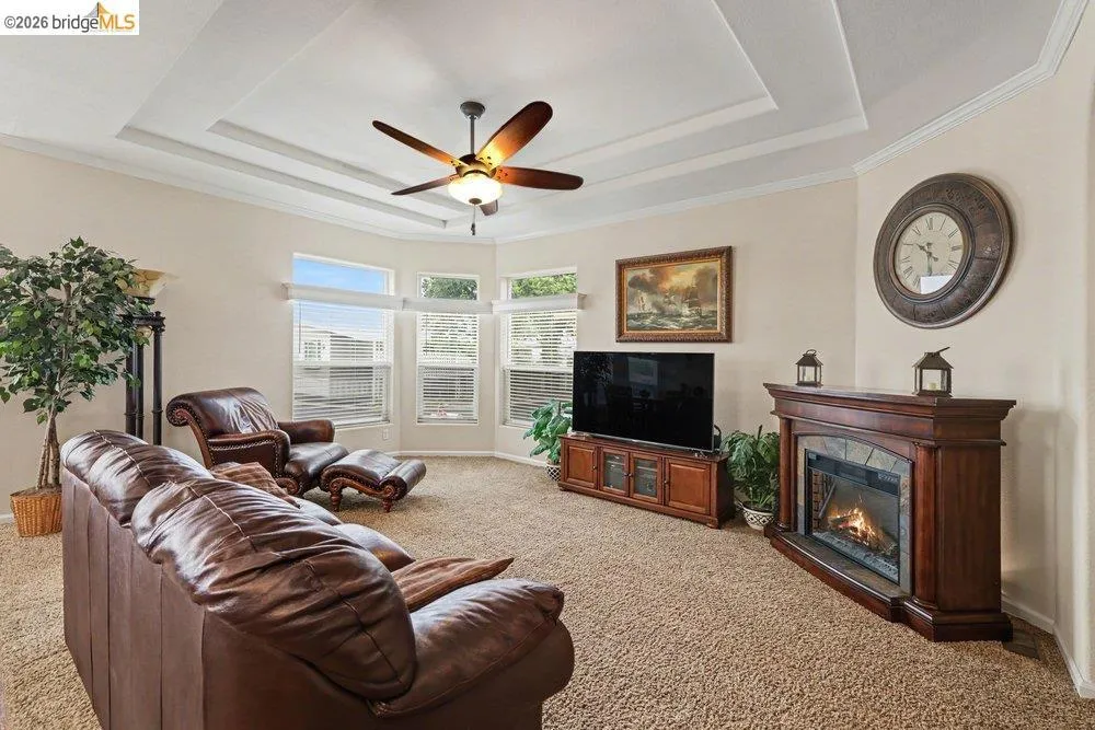 Living room with light carpet, ceiling fan, crown molding, and a premium fireplace Living room with light carpet, ceiling fan, crown molding, and a premium fireplace
